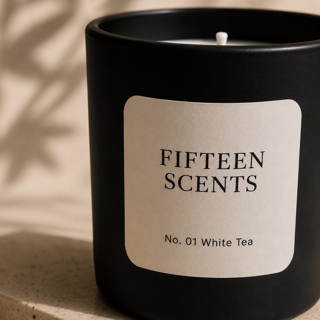 Black candle with a beige label reading 'Fifteen Scents No. 01 White Tea' on a neutral background.